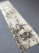 Light beige runner rug with dark speckled abstract strip pattern, short plush pile