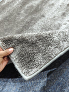 Dark gray runner rug with low pile texture and stitched border, corner folded up