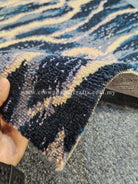 Hand-held close-up of wavy patterned runner rug fibers in dark navy and light beige.