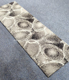 Diagonal view of abstract runner rug with oval and circular linework on beige-gray