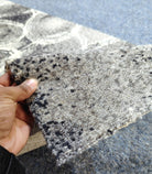 Hand-held runner rug corner showing speckled pattern and abstract circles in gray