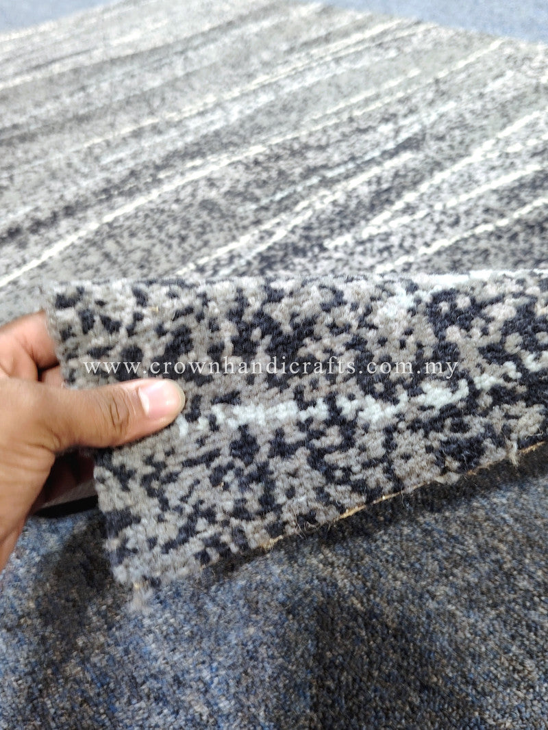 Hand holding rug corner; cream with dark blue-black speckled horizontal stripes