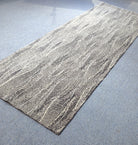 Abstract floor runner rug, beige with flowing line texture and dark speckled edge.