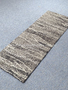 Beige abstract runner rug with thin dark horizontal stripes, angled top view