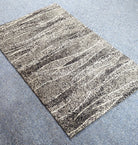 Abstract area rug with beige and dark speckled horizontal lines, angled view