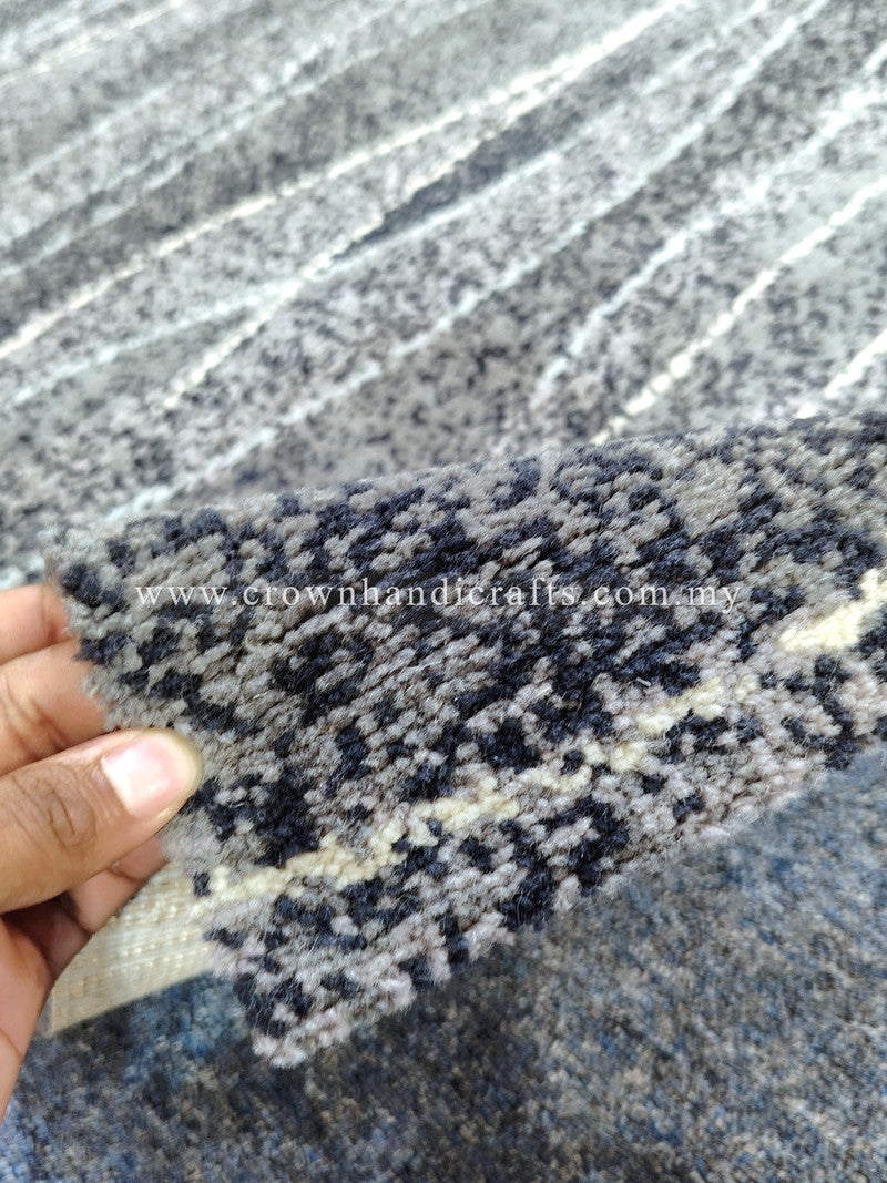Abstract area rug with navy-gray and white speckled stripe pattern, hand holding corner