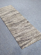 Runner rug: beige-and-black speckled abstract bands, textured flat weave, angled.