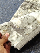Compact grey mat rug, beige pile with distressed dark pattern; close-up edge view