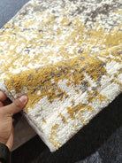 Two-tone runner rug corner with grey and yellow abstract distressed weave, held by hand