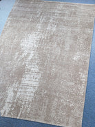 Abstract area rug with distressed beige and white texture, corner edge visible.