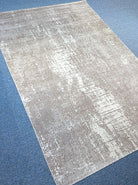 Abstract area rug with worn beige and white abstract strokes, diagonal view.
