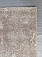 Abstract area rug with distressed beige and white pattern and stitched edge.