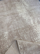 Abstract area rug with distressed beige and white design, rolled corner visible.