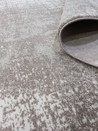 Abstract area rug with distressed beige and white pattern, rounded rolled edge.