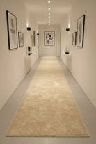 Long hallway with a beige runner rug, white walls, and framed art.
