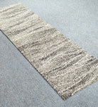 Narrow runner carpet with beige base, dark speckled horizontal stripes, angled view.