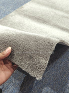 Grey cut-pile runner rug edge detail with dense textured fibers, hand holding corner