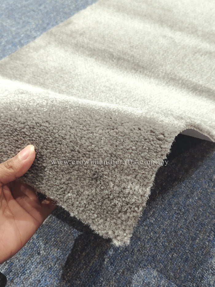 Grey cut-pile runner rug edge detail with dense textured fibers, hand holding corner