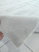 Oatmeal-beige rug corner with thick plush pile and hand holding edge
