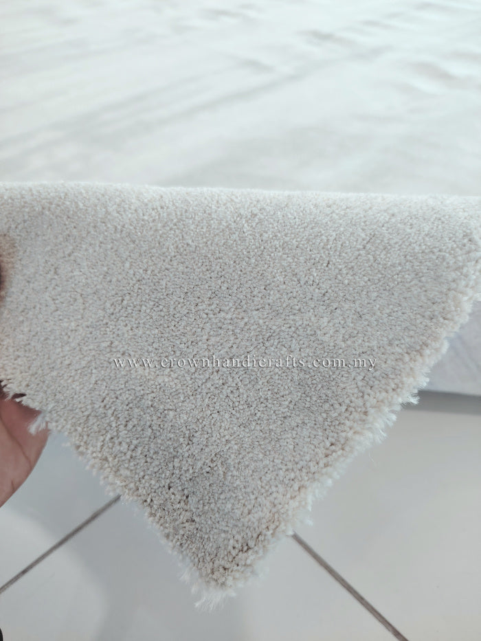 Oatmeal-beige rug corner with thick plush pile and hand holding edge
