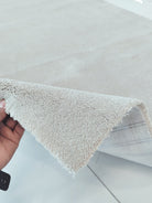 Oatmeal beige area rug edge held up, showing short fringe and soft shag pile