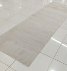 Oatmeal beige long runner rug with low, even pile; plain surface and short fringe.