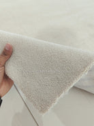 Oatmeal beige runner rug corner with short fringe edge; hand showing the thickness.
