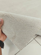Oatmeal beige runner rug corner with short fringe edge; hand holding the rug tip.