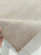 Shaggy accent rug with short plush pile, light beige color at a corner edge