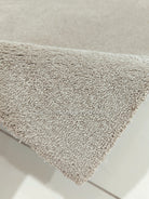 Shaggy rectangular rug, light brown with short dense pile and neatly bound edges.