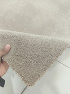 Light brown shaggy square rug with plush pile edge, held by hand for texture detail