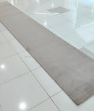 Taupe long shaggy runner rug laid on tile floor, wide rectangular shape