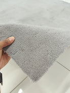 Grey shaggy floor rug corner, dense soft pile with neatly trimmed edge.
