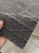 Dark grey rug edge close-up in hand; textured grid weave and trimmed border