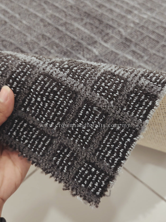 Dark grey rug edge close-up in hand; textured grid weave and trimmed border